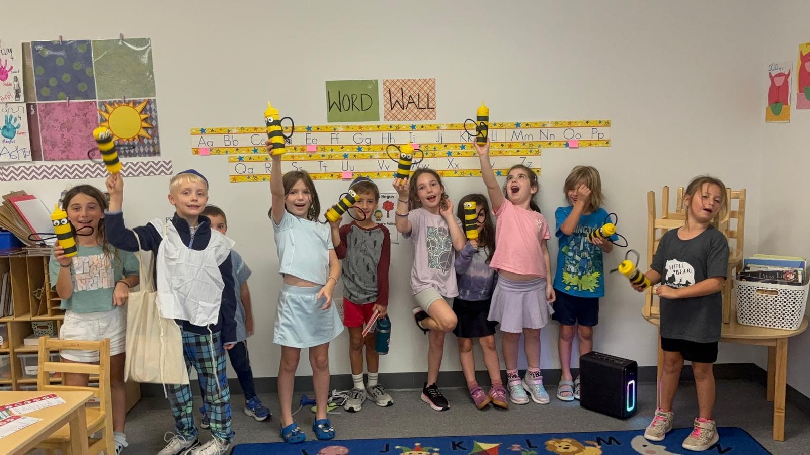 Children cheering with handmade bumblebee crafts under a word wall
