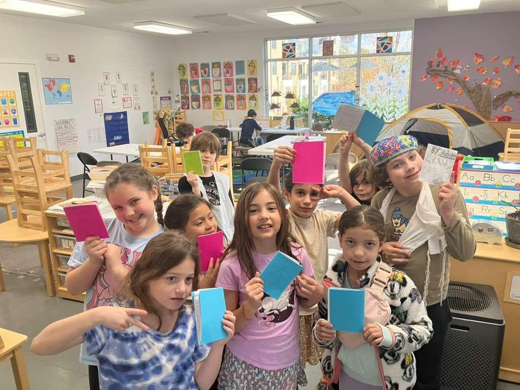 Children in a bright classroom holding up handmade booklets
